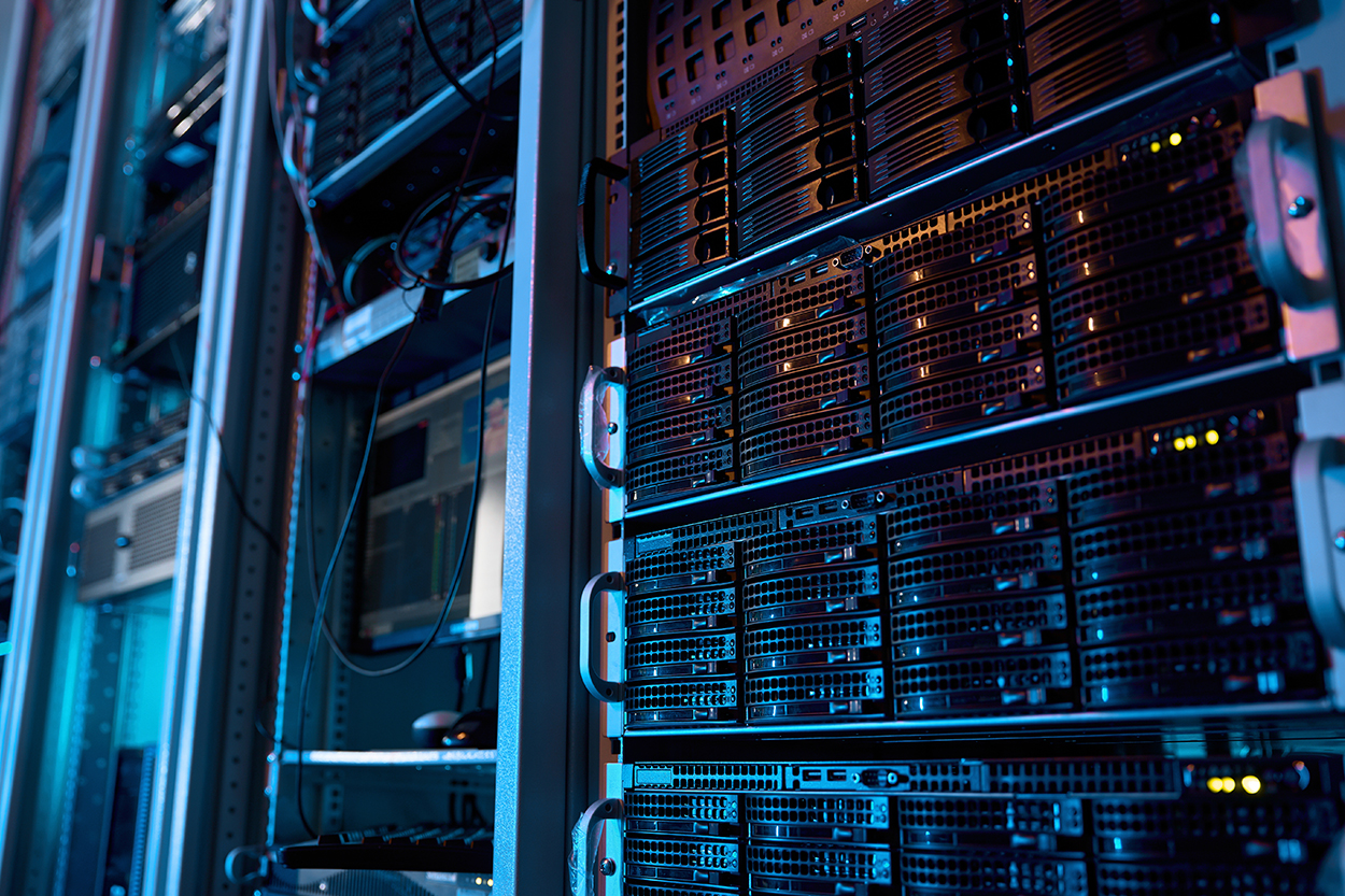 Nahaufnahme eines beleuchteten Serverraums mit mehreren Racks, Datenkabeln und leuchtenden Anzeigen
