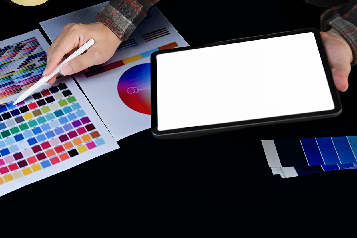 Tablet mit leerem Bildschirm, Farbpaletten und Farbmusterbogen auf dunklem Tisch.