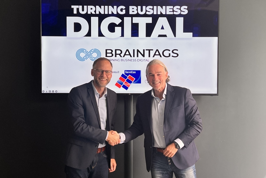 Servicon- und Braintags-Geschäftsführer schütteln sich die Hand vor einem Bildschirm mit Turning Business Digital Schriftzug