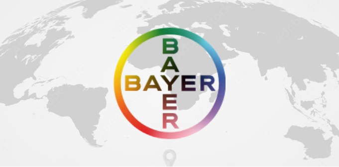Bayer-Logo mit farbigem Kreis in Regenbogenfarben und vertikalem sowie horizontalem Schriftzug Bayer vor einer Weltkarten-Silhouette.“